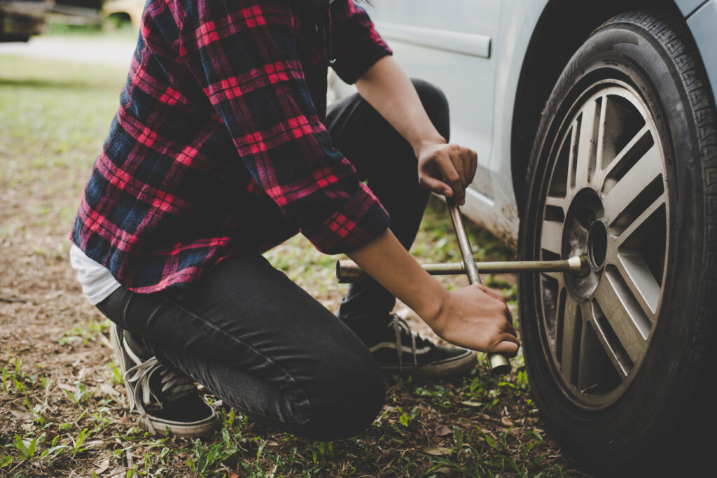 Uma jovem a verificar um pneu furado no seu carro e a tentar arranjá-lo.